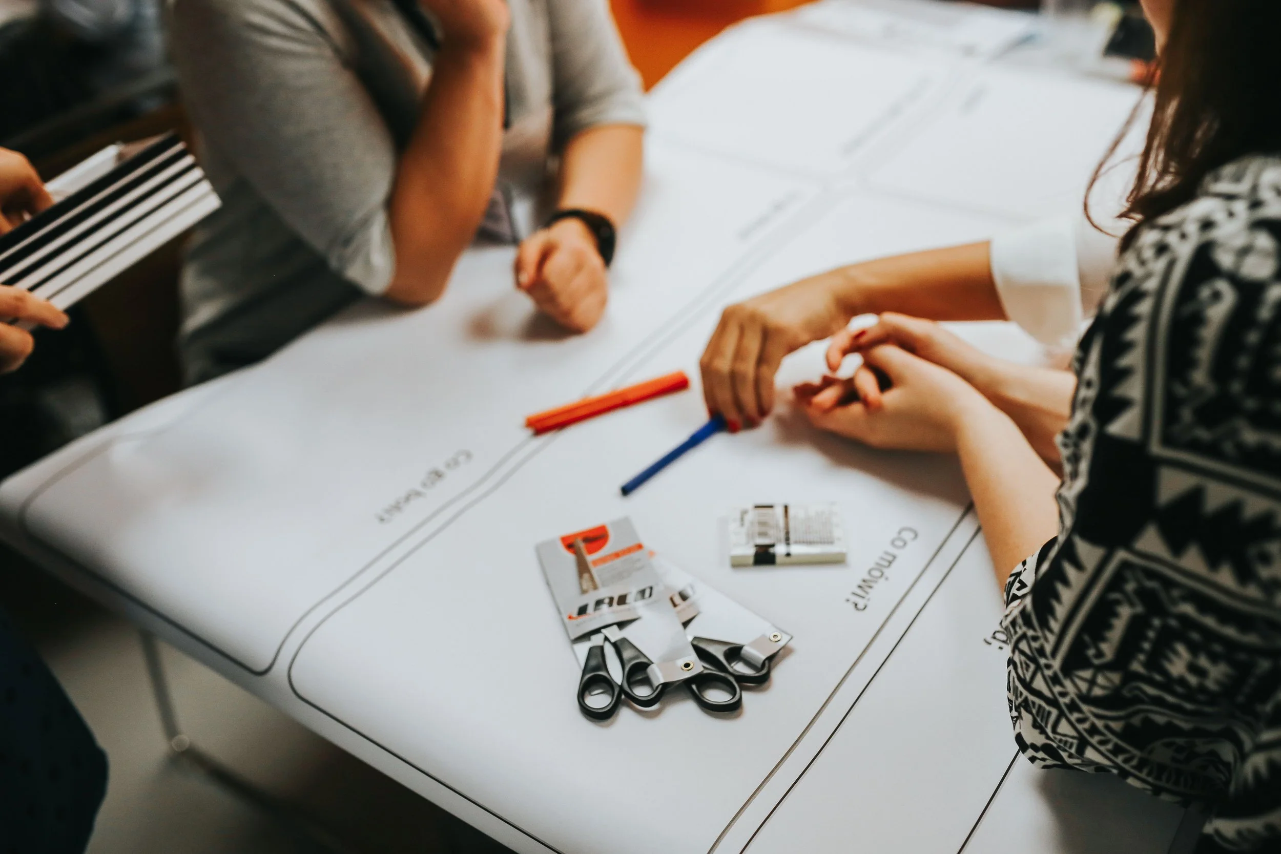 People sitting at a table engaged in a crafting activity, with scissors, glue, colored sticks, and paper on the table.