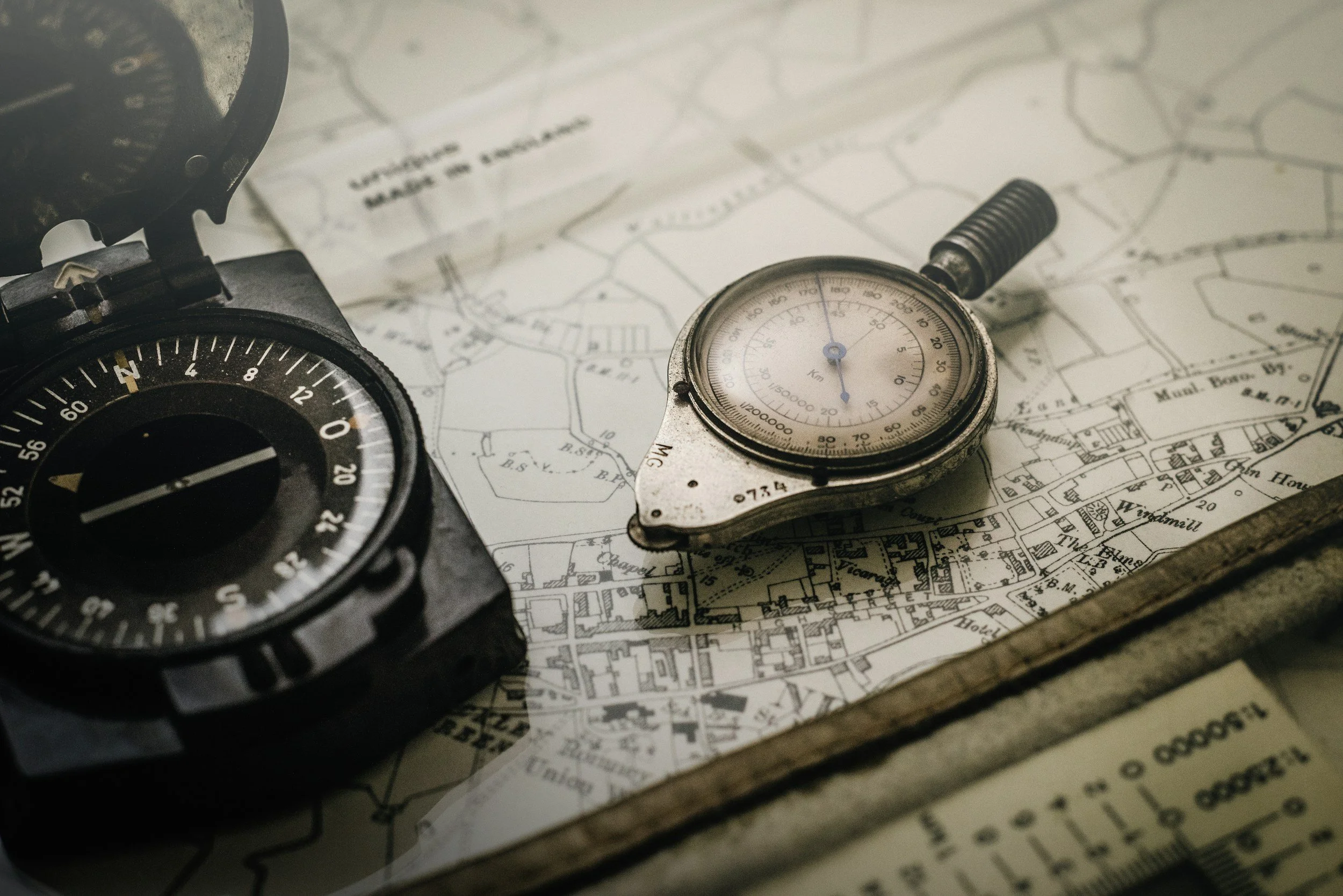 A compass and a stopwatch placed on a map, with the compass pointing north and the map showing detailed street layouts.