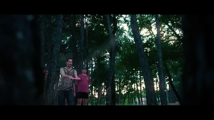 Three people walking through a dense forest with tall trees during daylight