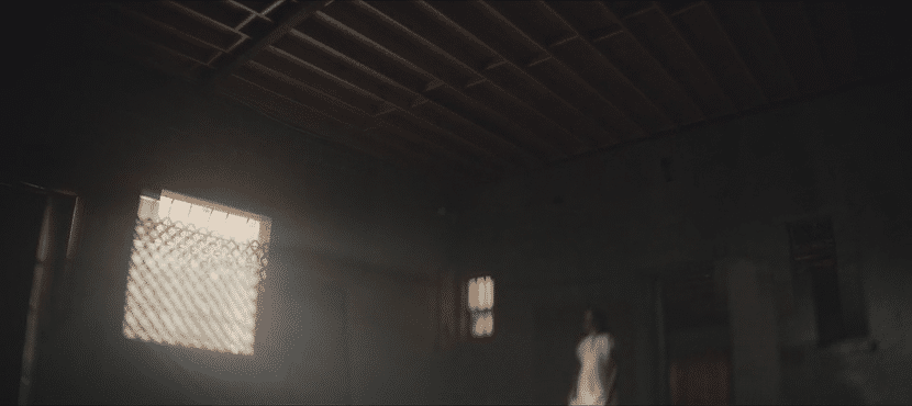 Interior of a dark room with sunlight shining through a window, a person standing in the background.