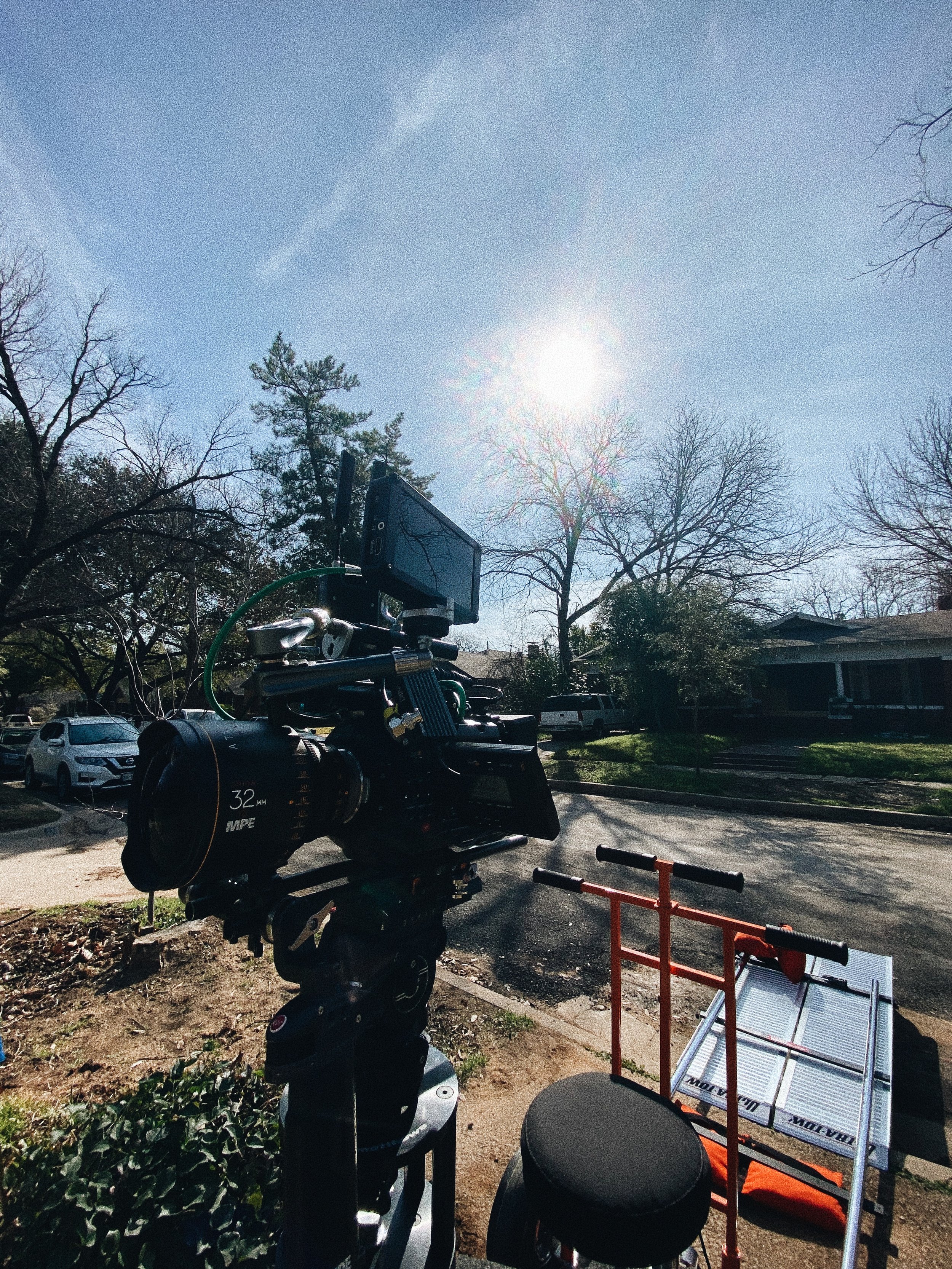 A professional film camera on a tripod outdoors on a sunny day, with a neighborhood in the background.