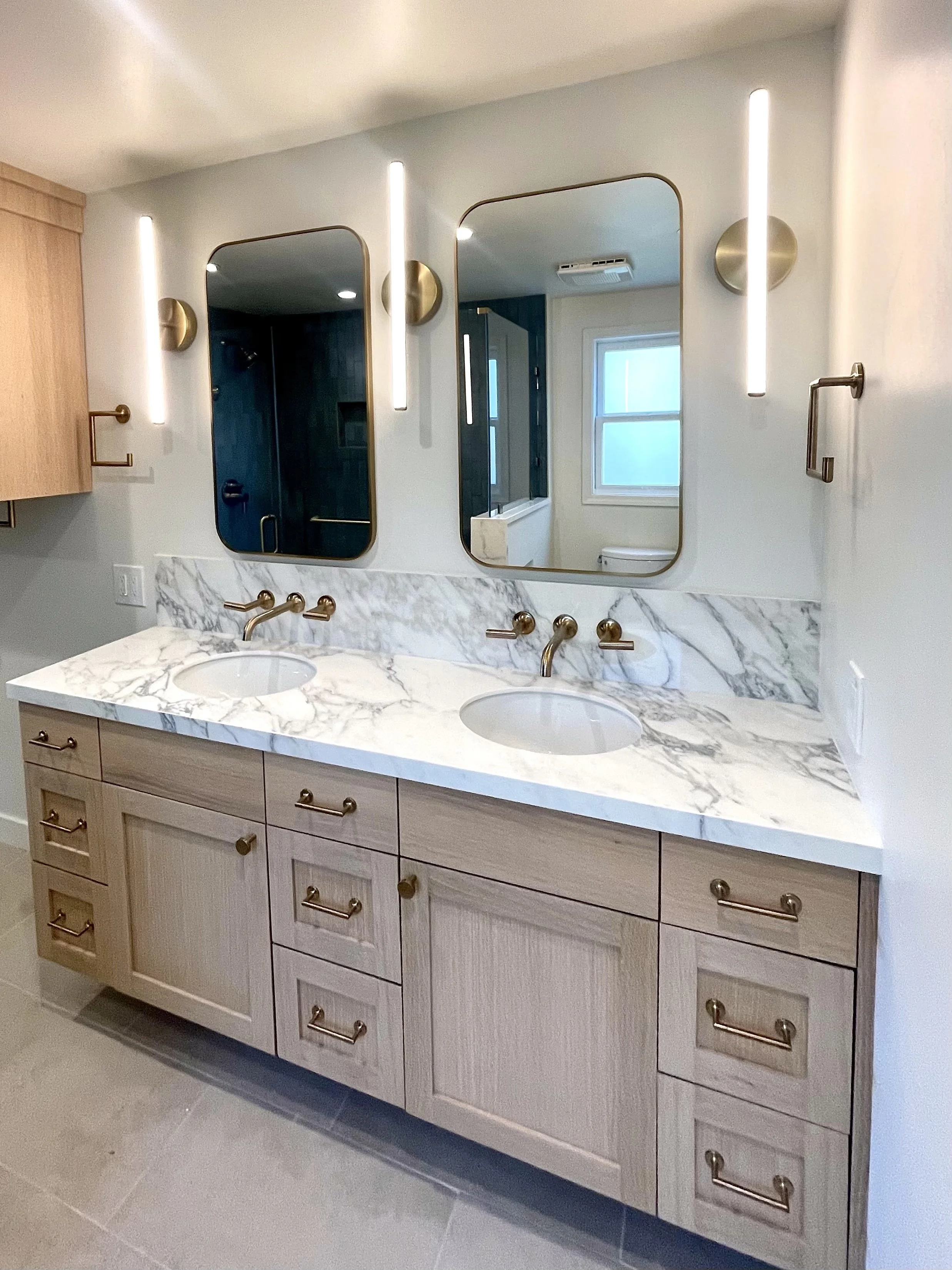 Bathroom vanity with double sinks, a marble countertop, and three mirrors above it, surrounded by modern lighting fixtures.