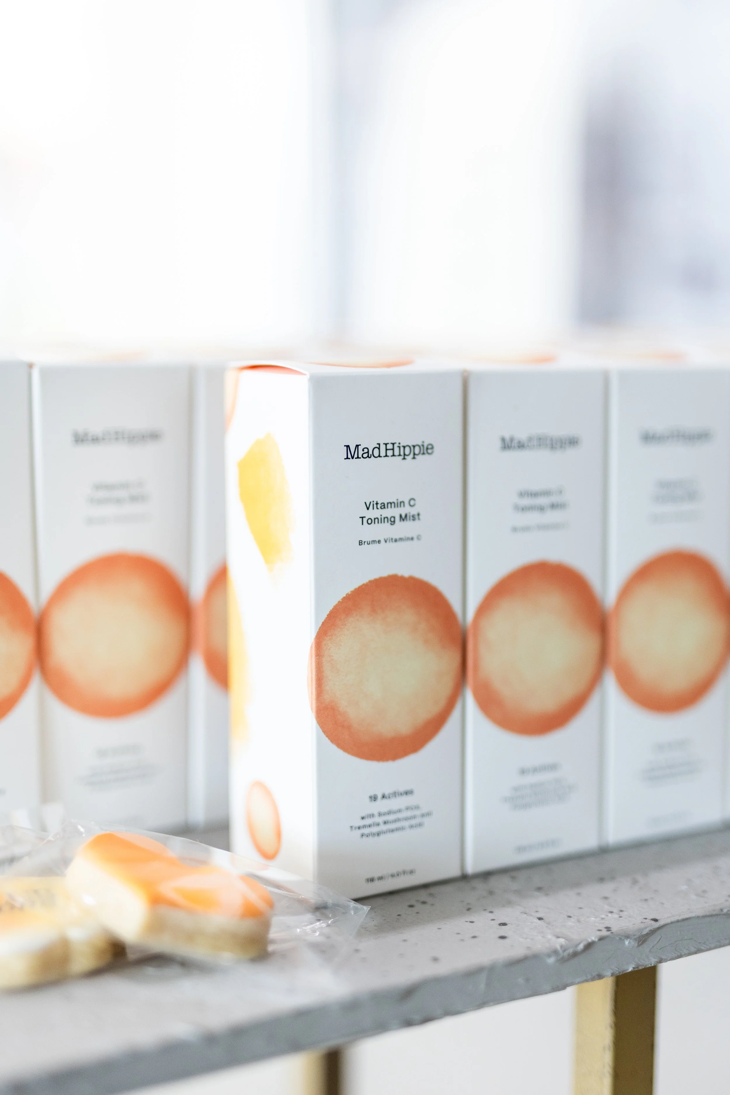 Boxes of MadHippie Vitamin C Toning Mist displayed on a shelf, with some small orange and white packaged products in the foreground.