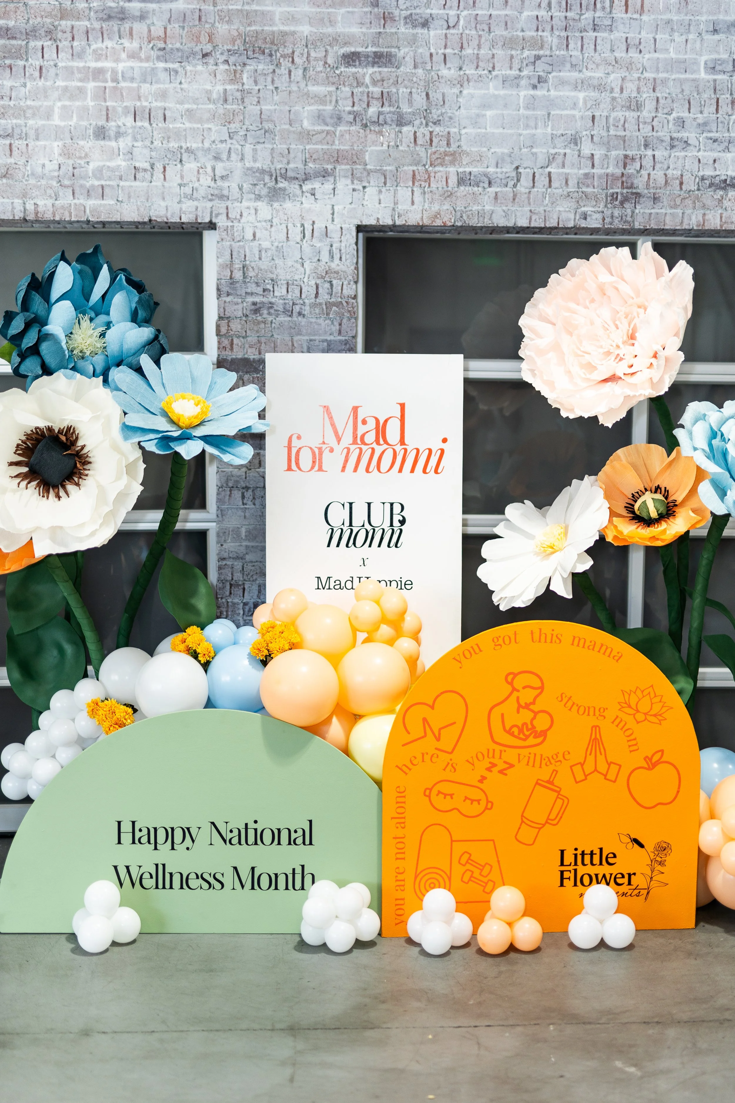 Decorative display celebrating National Wellness Month, featuring paper flowers, balloons, and signs with messages about motherhood and wellness.
