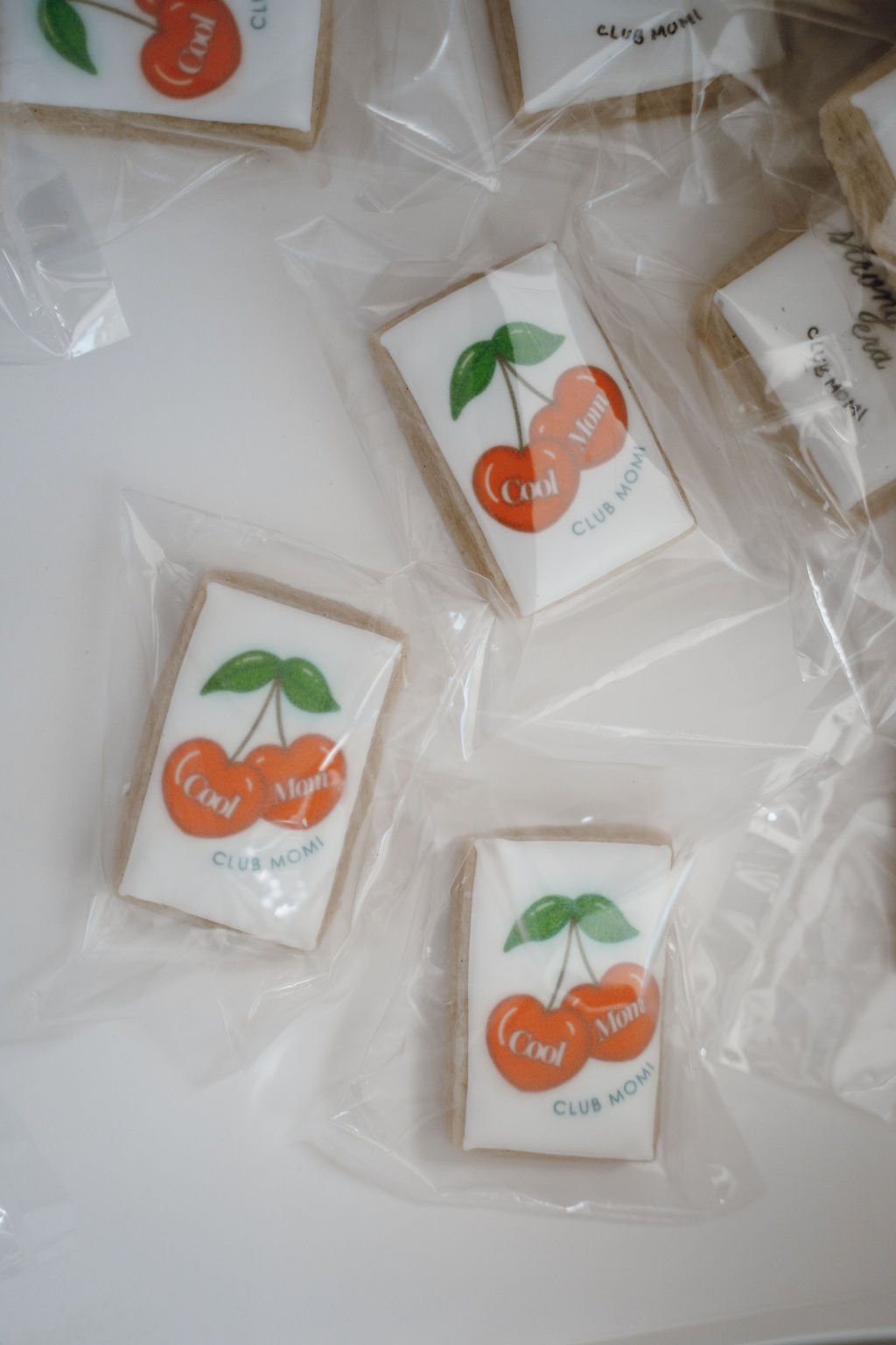 Cookies with cherry and leaf design, wrapped in clear plastic, with text reading 'Cool' and 'Club Momi'