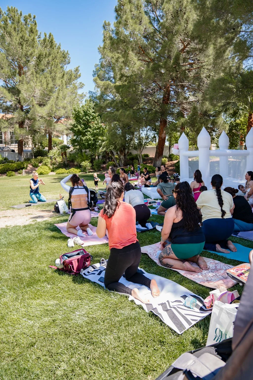 People participating in an outdoor yoga or meditation class on a grassy area surrounded by trees, with a white inflatable structure in the background.