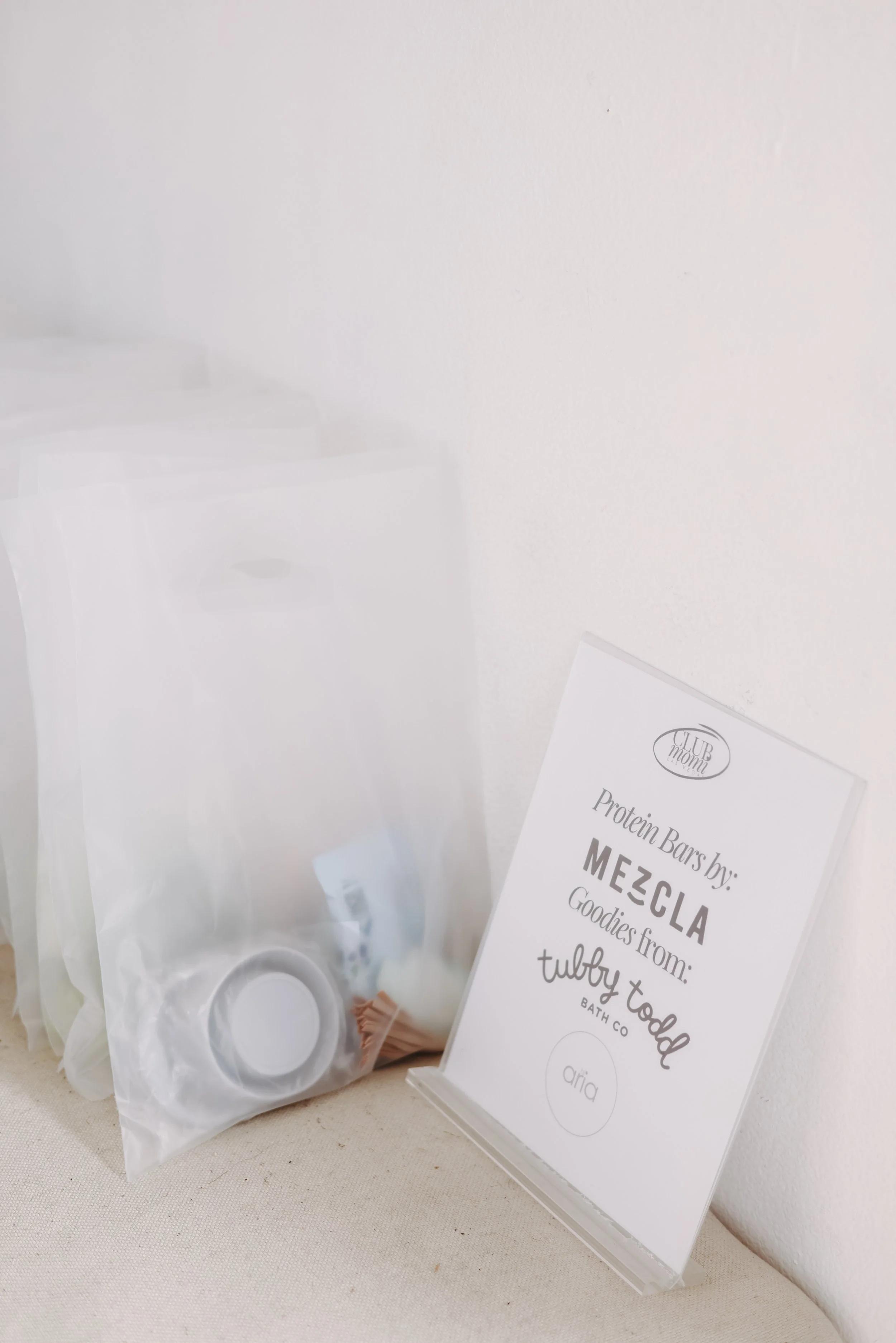 A clear plastic bag containing personal care items, and a white sign with black text about protein bars from Mezcla, a bath company