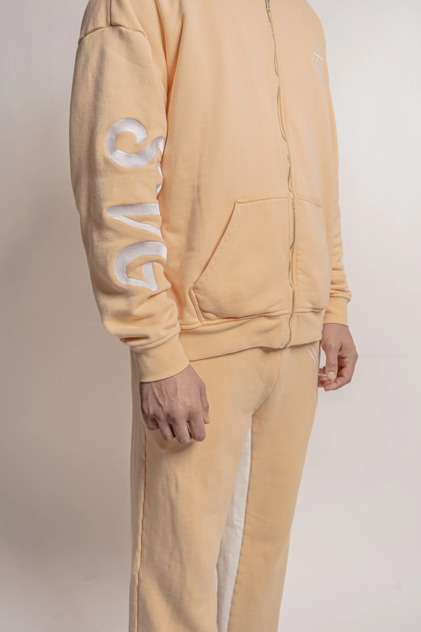 Person wearing a light peach-colored Champion hoodie and matching sweatpants, standing against a plain background.