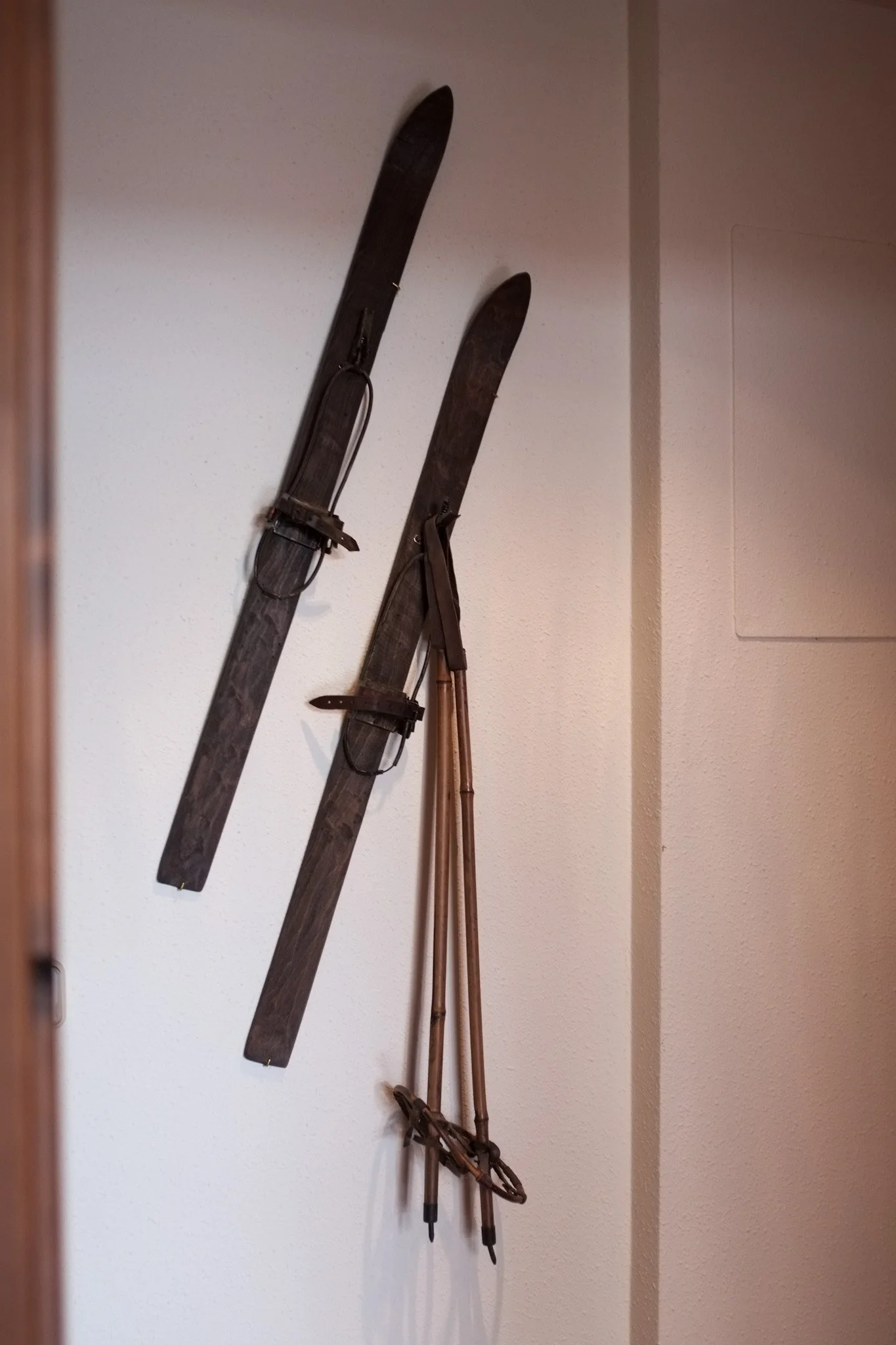 Un par de esquís antiguos negros con correas y unas botas de esquí de madera colgados en la pared.