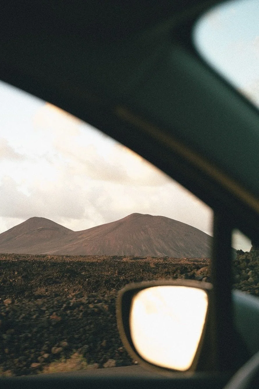 Vista de un volcán en un paisaje desértico, visible desde el interior de un automóvil, con el espejo retrovisor en primer plano.