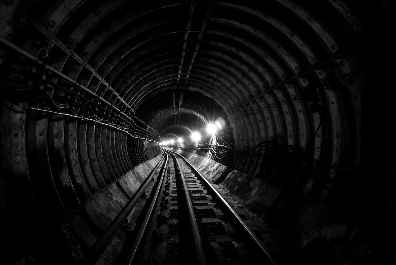 Vista de una vía del tren en un túnel oscuro con luces al fondo
