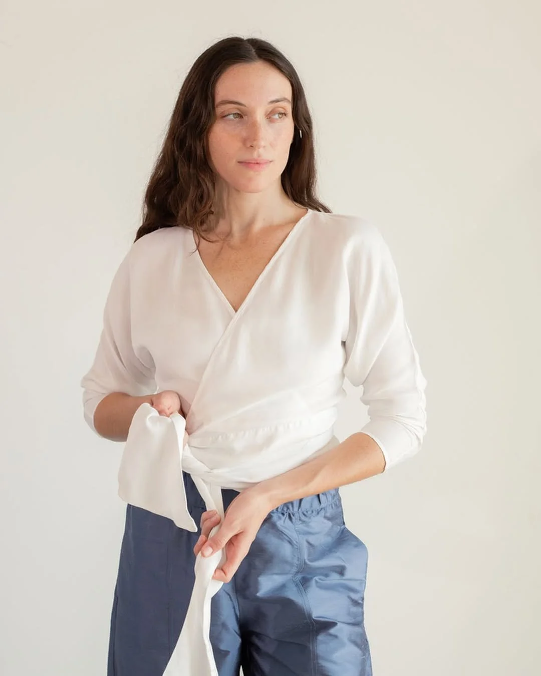 Mujer joven con blusa blanca y pantalones azul oscuro, mirando hacia la izquierda.