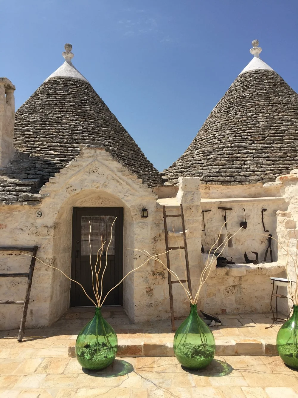 Casas tradicionales con tejados cónicos de piedra, decoradas con macetas verdes y utensilios de agricultura en un día soleado.