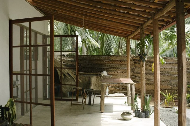 Porche de madera con mesas y sillas, en un entorno natural con plantas tropicales.
