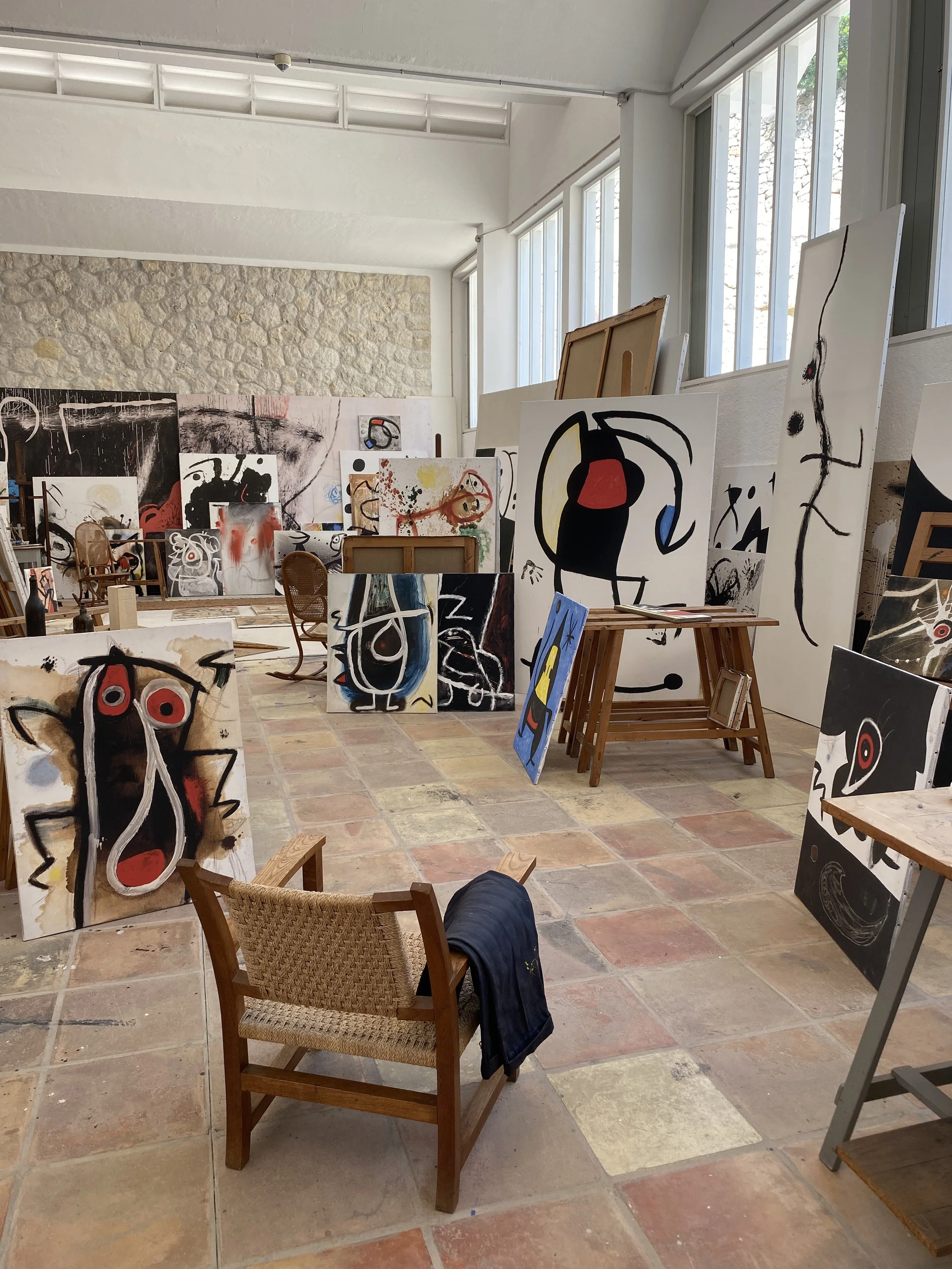 Varios cuadros abstractos en un taller de arte, con una silla de mimbre y un vestido colgado