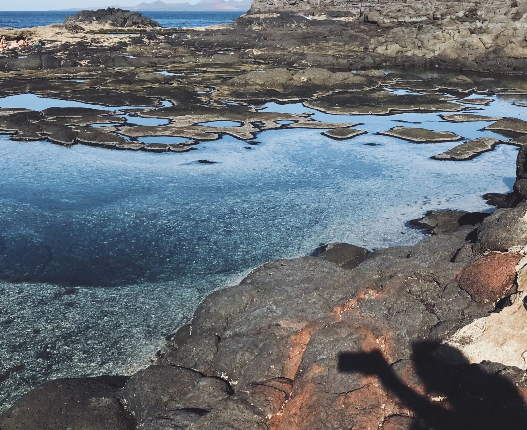 Un cuerpo de agua con varias piscinas naturales formadas por rocas volcánicas en la costa, con el agua reflejando el cielo y algunas rocas en la orilla.