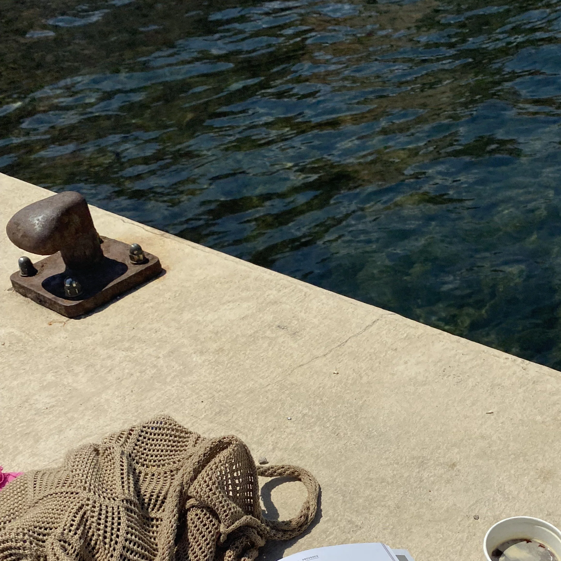Borde de muelle con una rosca de amarre, una red de pesca, una taza con café y un libro, junto a agua del río