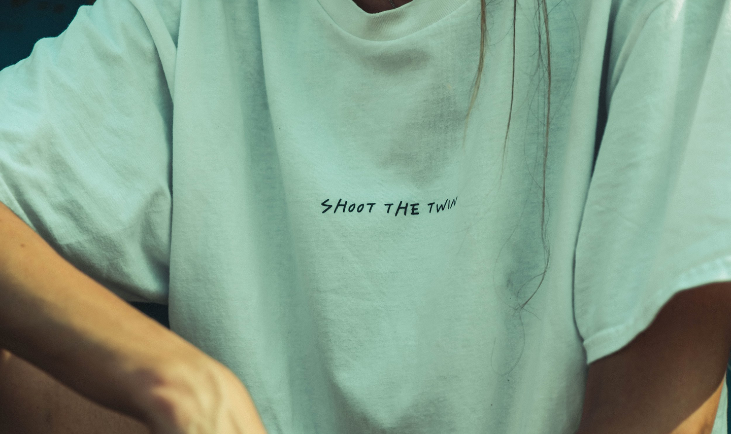 Persona con camiseta verde que dice 'Shoot the Twin' en el pecho.