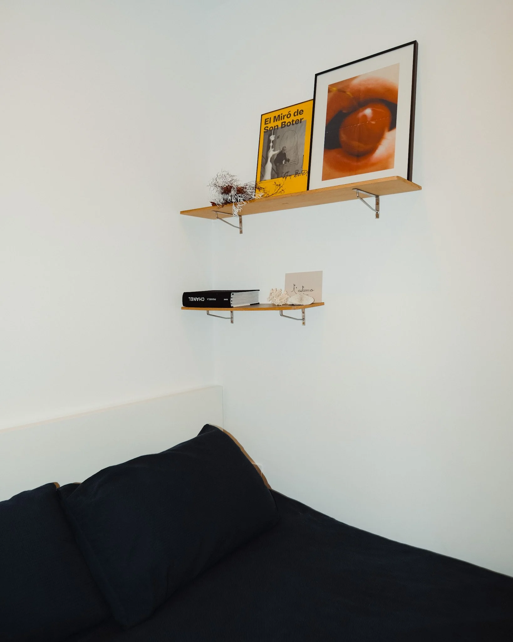 Estantes con libros, carteles y decoraciones en una pared blanca sobre una cama con cobijas negras.