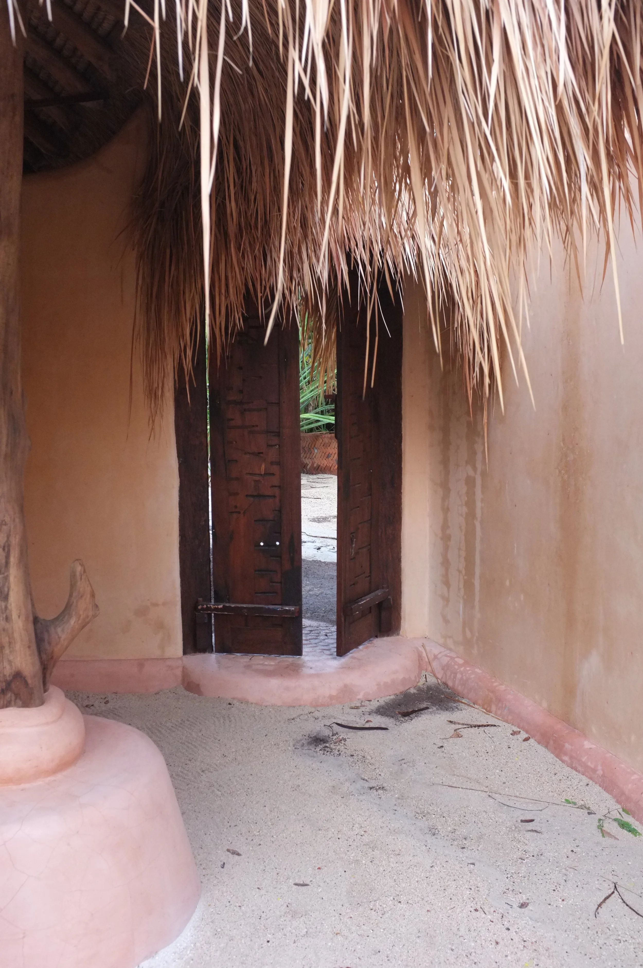Puerta de madera en un muro de barro con techo de paja