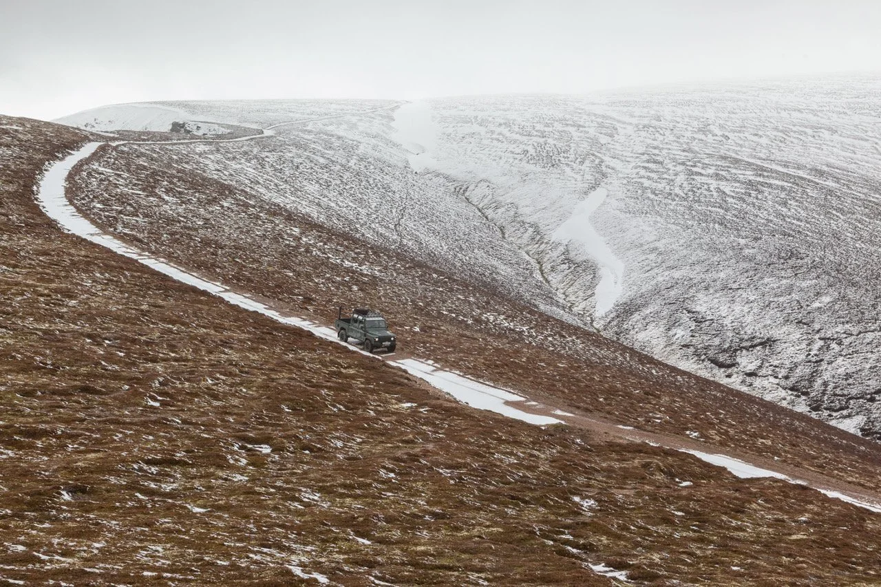 Un vehículo en un camino de tierra en una colina con nieve en un paisaje montañoso.