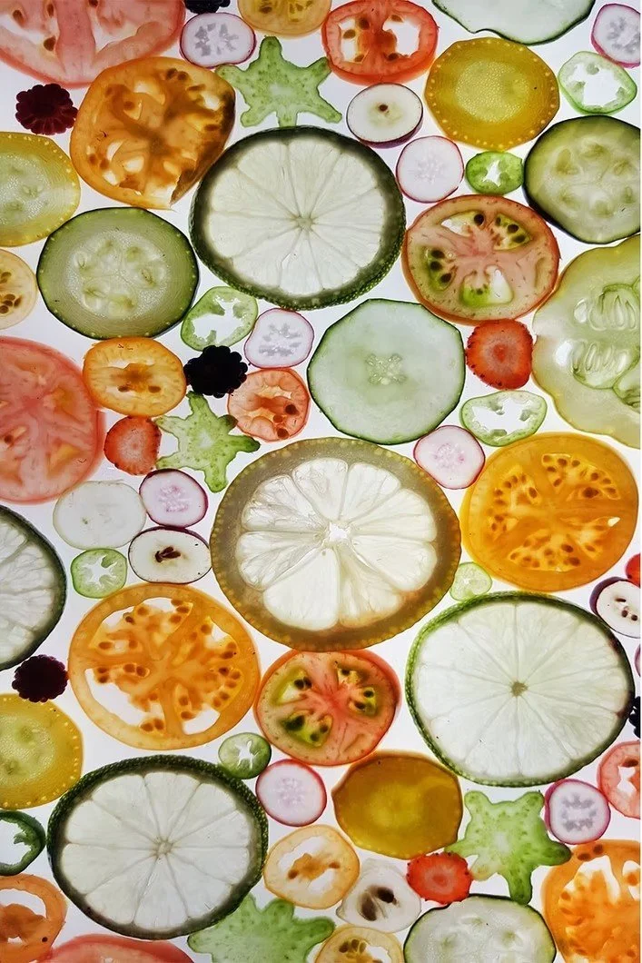 Variedad de rebanadas de diferentes frutas como pepino, tomate, limón, cebolla, fresa, y otras, dispuestas en un fondo de luz.