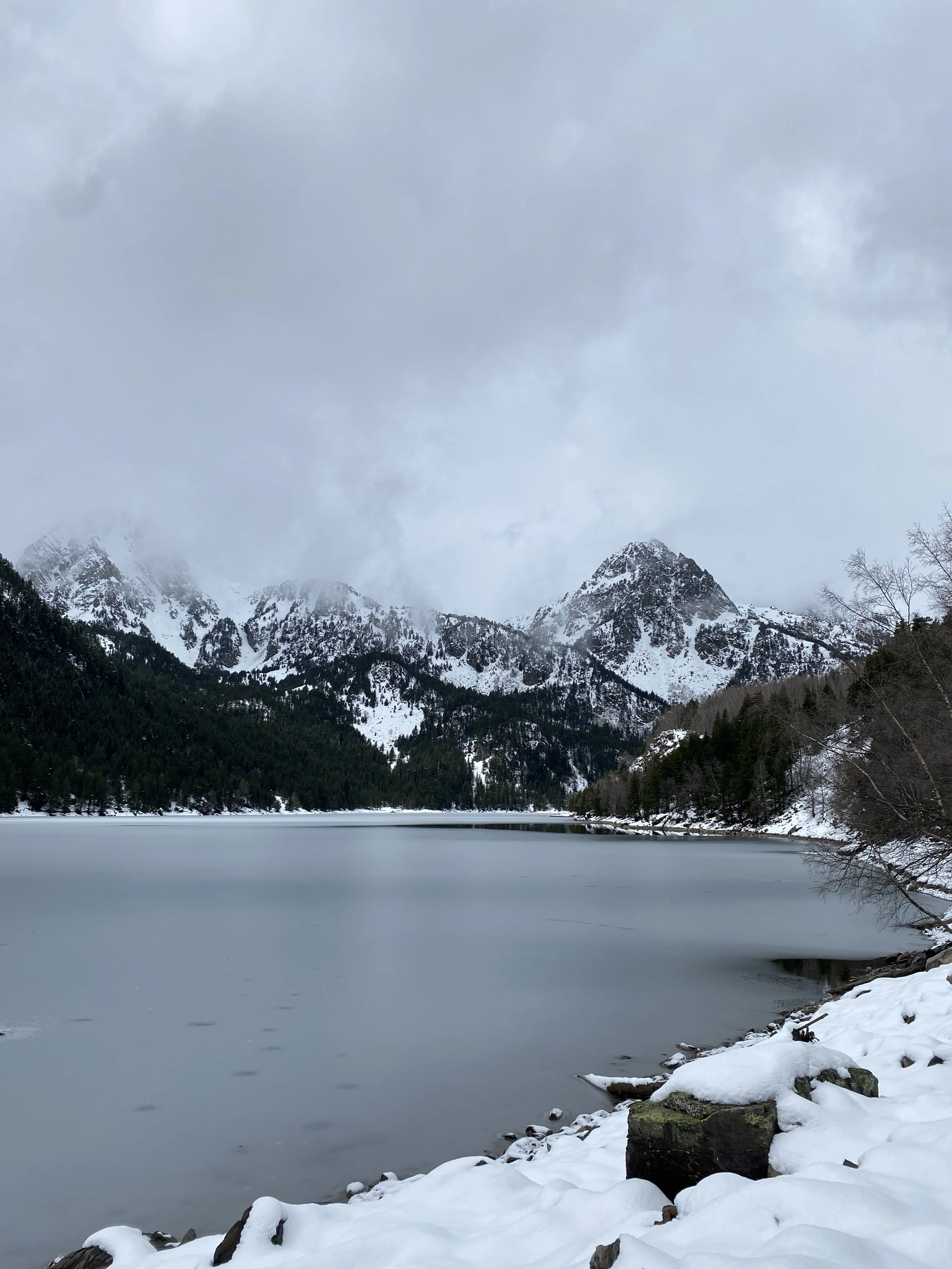 Lago en las montañas con nieve y árboles, nubes en el cielo, paisaje invernal.