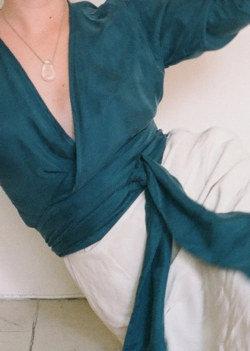 Mujer con blusa azul, pantalones blancos, y collar de perla