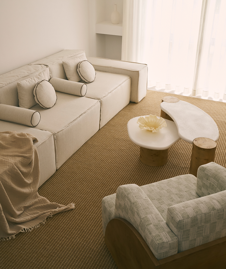 Sala de estar con sofá blanco, sillón gris, mesa ovalada con decoración de concha, cortinas blancas y alfombra a rayas.
