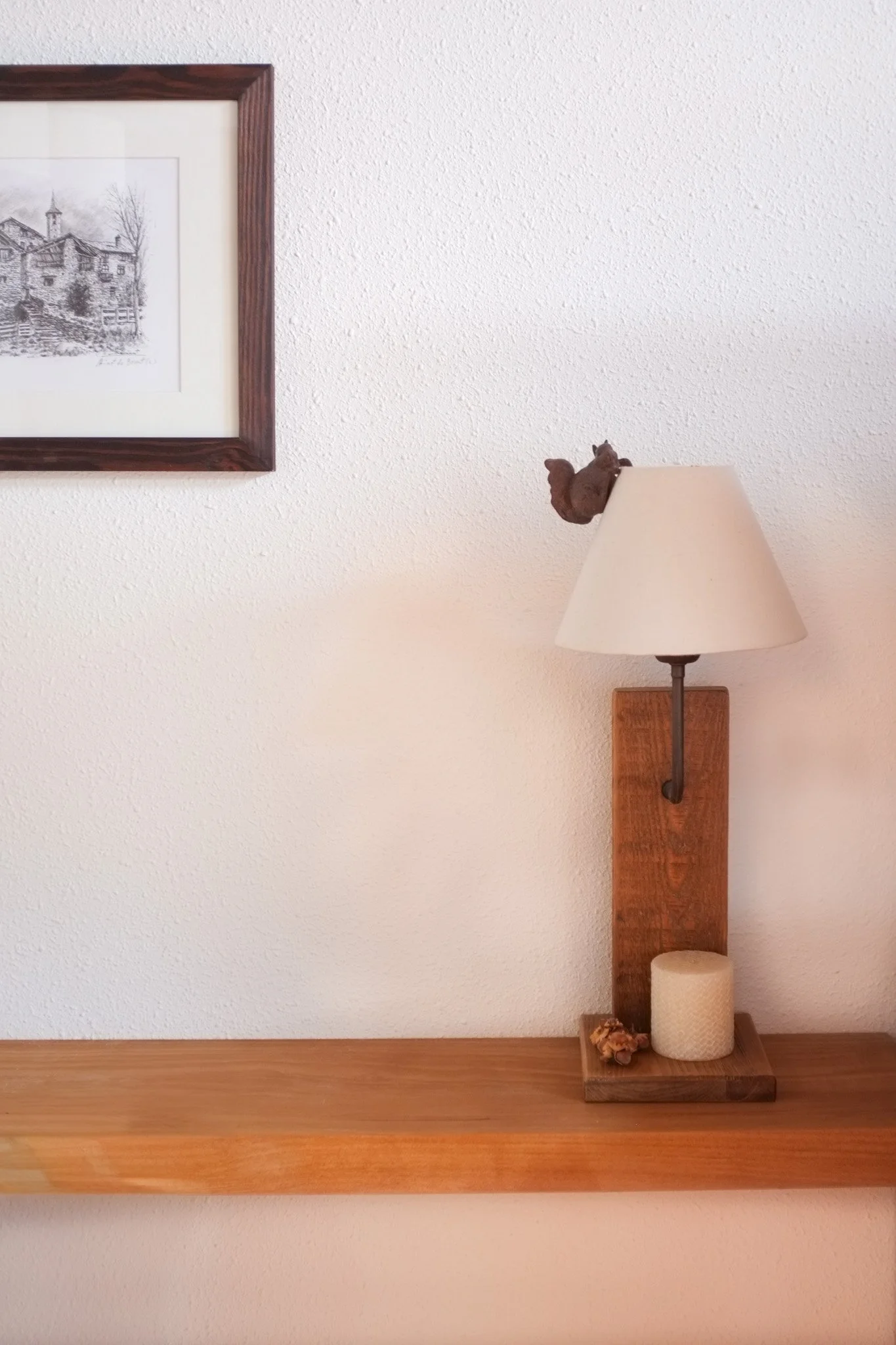 Una lámpara de pared con base de madera, con una pequeña figura de un ardilla en la parte superior, y una base de encendedor y una piña en la repisa de madera.