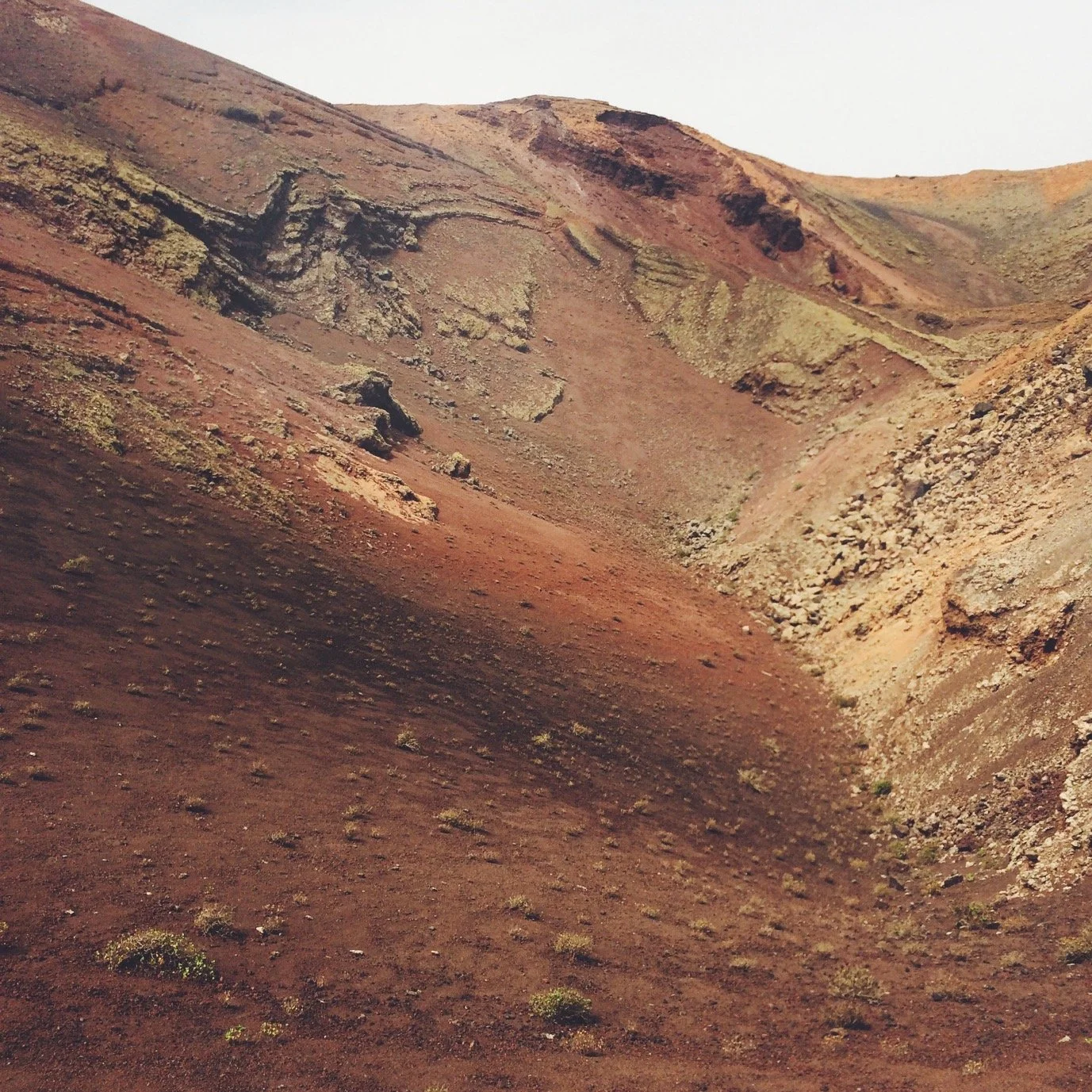 Paisaje de colinas con tierra de color rojo y algunas plantas pequeñas dispersas.
