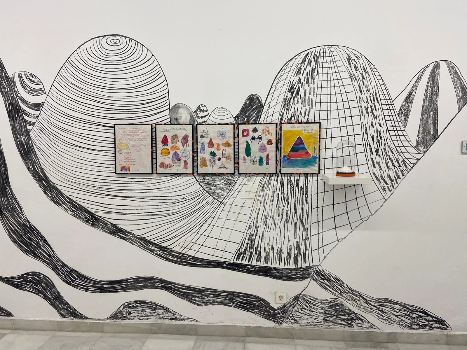 Mural en blanco y negro de montañas, con cuatro cuadros de arte infantil y una escultura en una repisa
