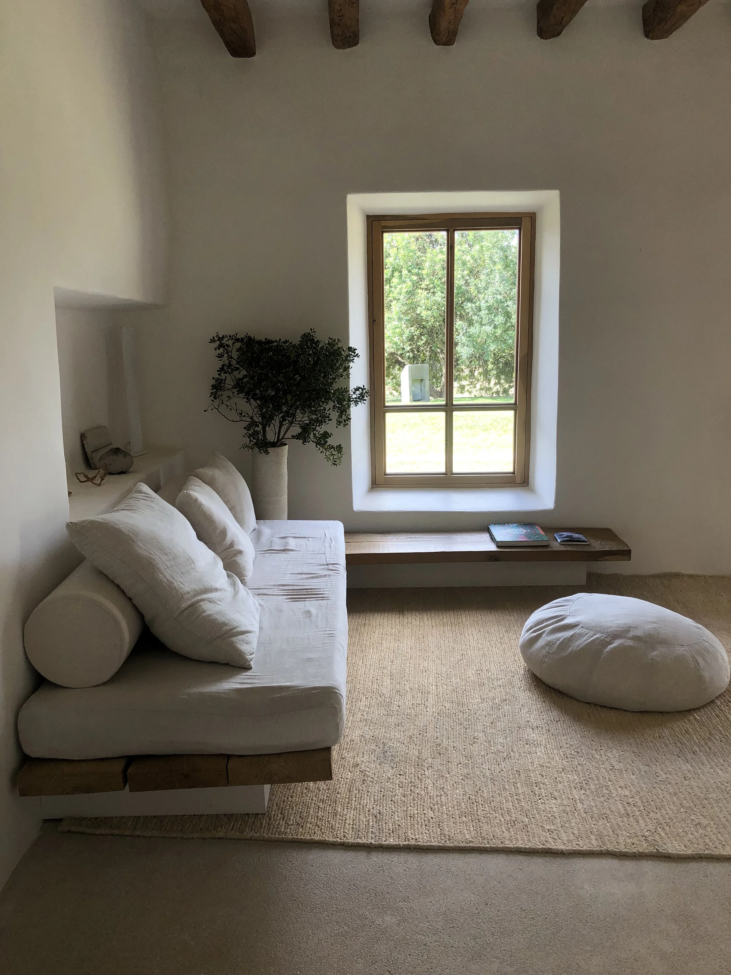 Sala sencilla con sillón blanco, pufs, ventana y plantas decorativas.