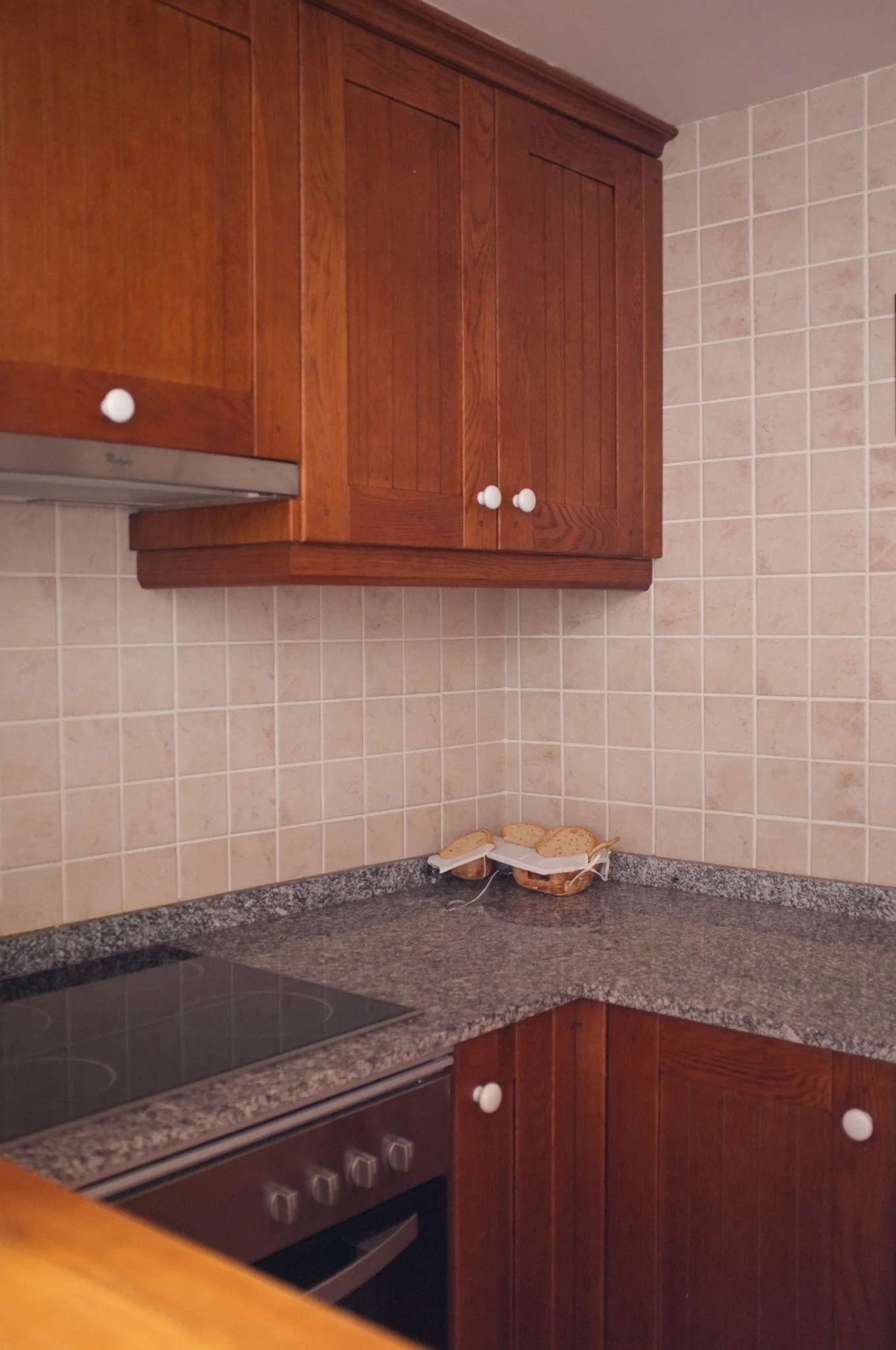 Cocina con gabinetes de madera, estufa y encimera de granito, y una cesta con pan en la esquina del mostrador.