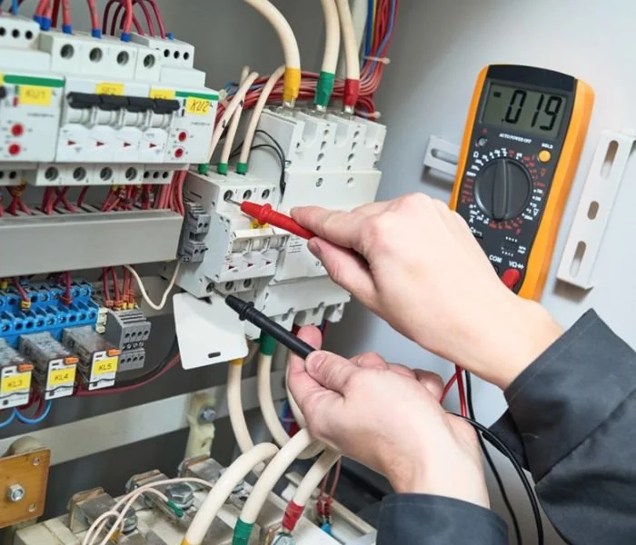 Person testing electrical circuit breaker with a multimeter in an electrical panel.