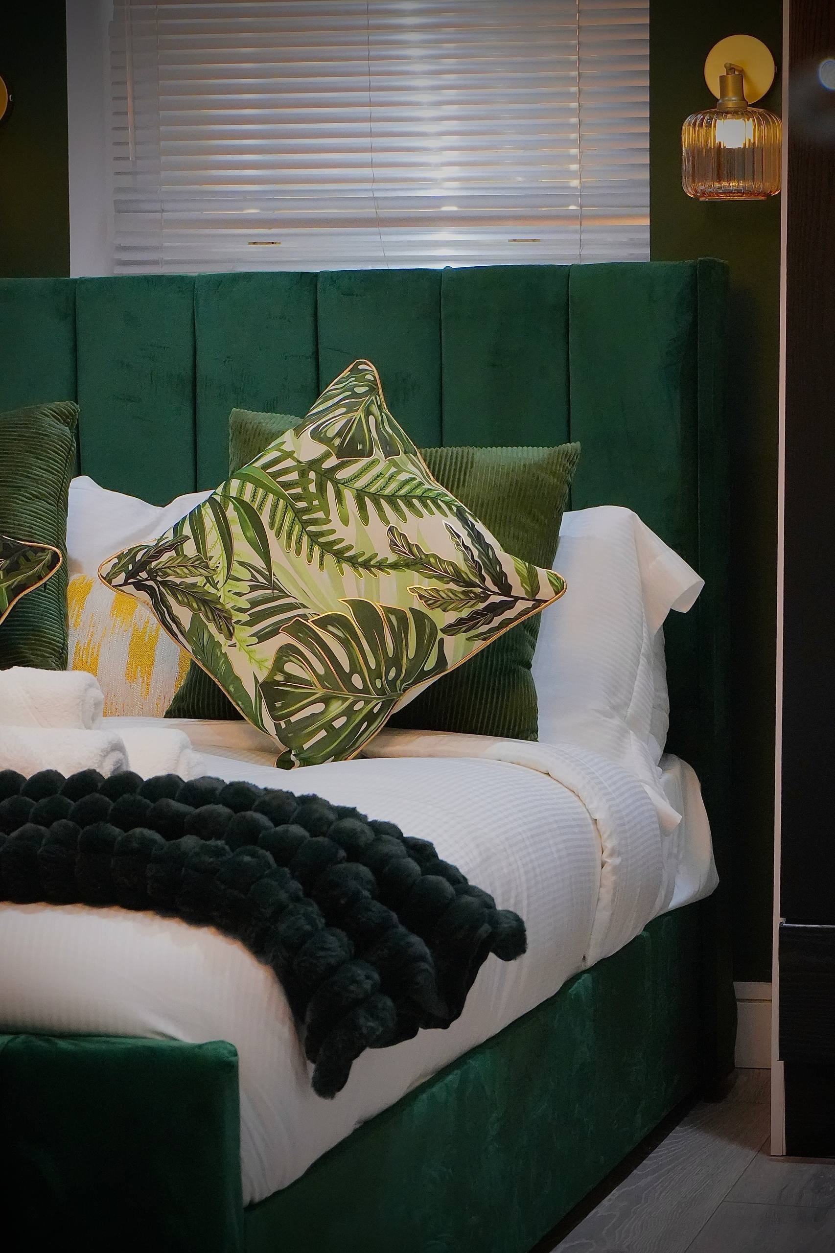 Two neatly made beds with white linens, a bedside table with a lamp, framed art, and a small vase with lavender. Towels with toiletries are arranged on the bed.