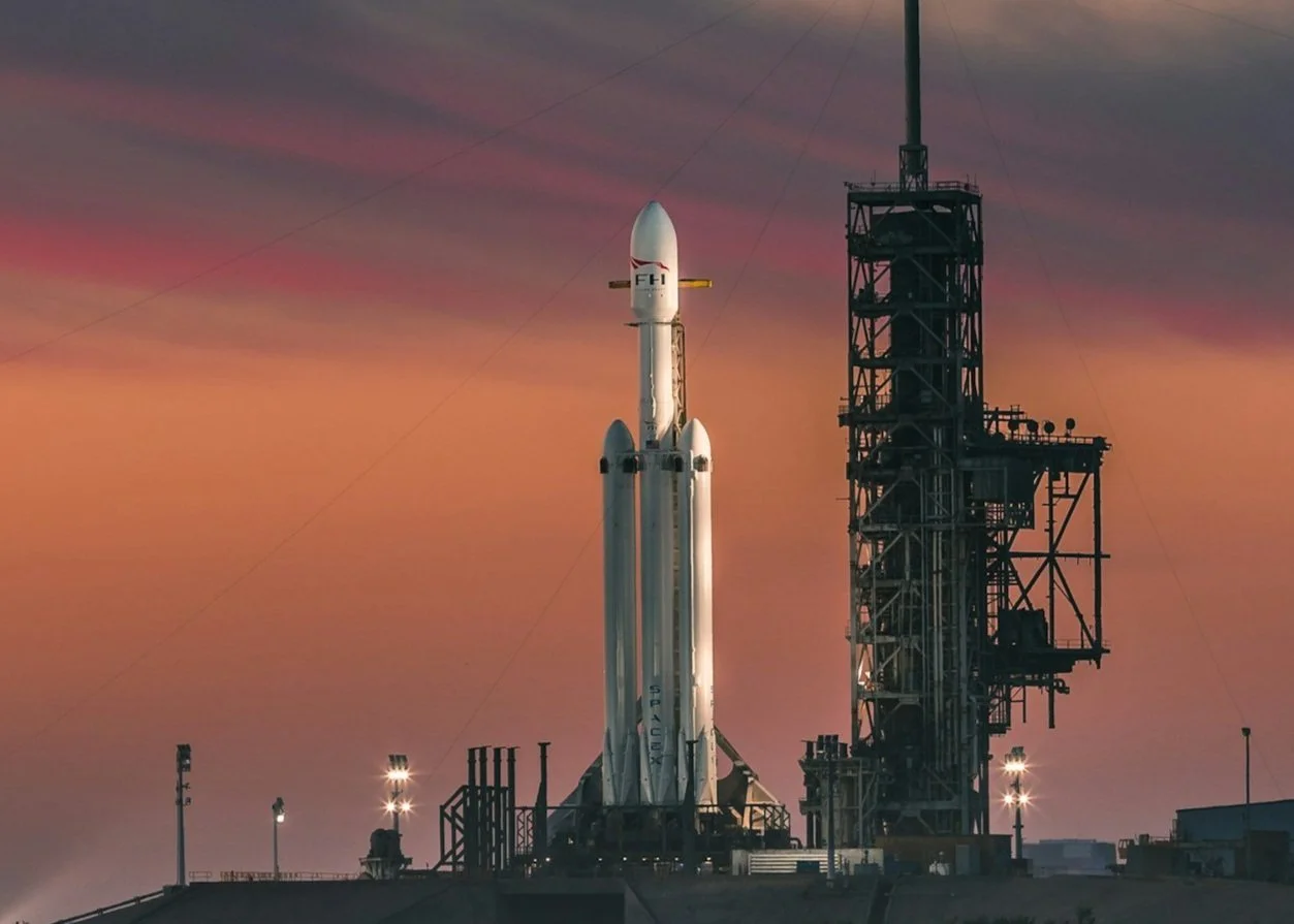 A rocket ready for launch on a launch pad against a vibrant sunset sky.