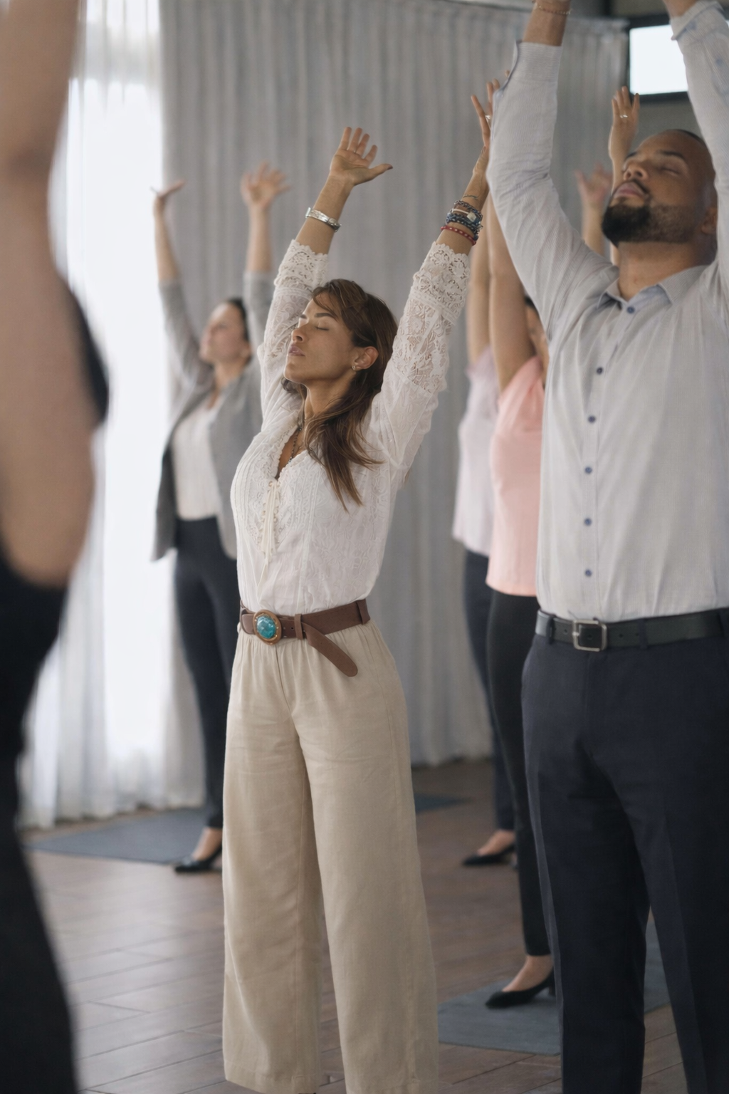 Grupo de personas en un encuentro de liderazgo consciente realizando una práctica de respiración y movimiento con los brazos elevados, promoviendo bienestar, presencia y conexión en un entorno corporativo.