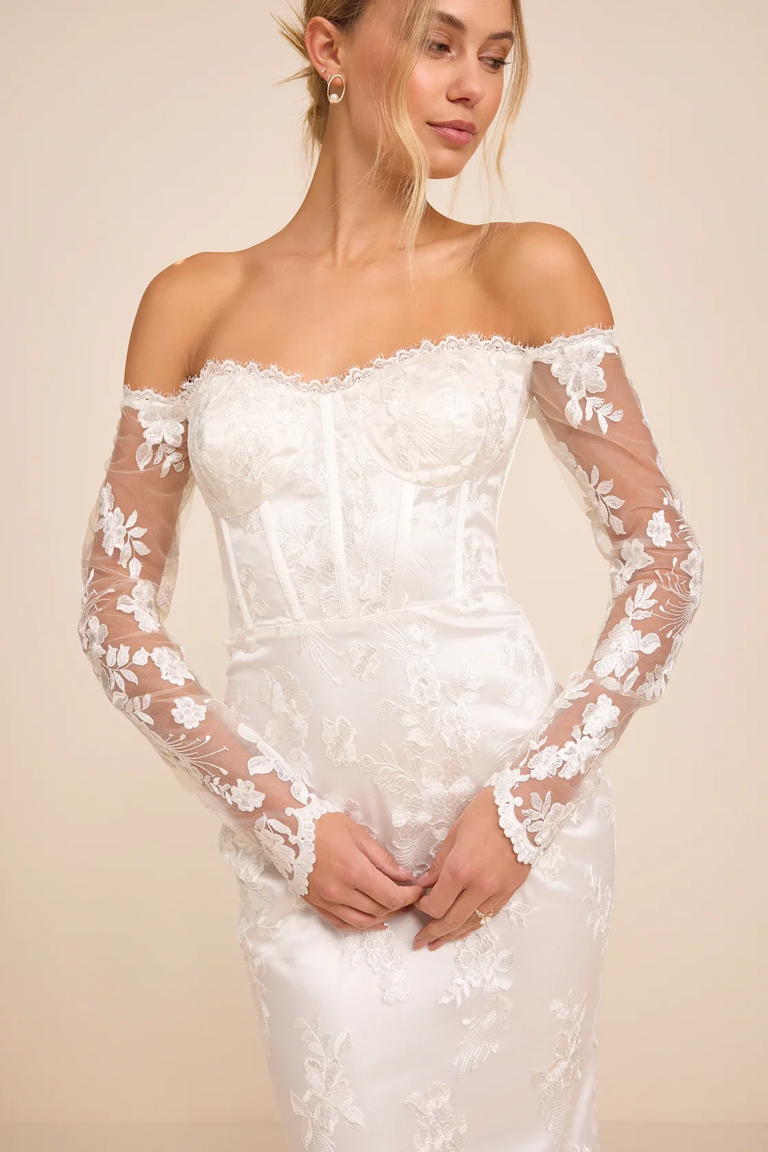A woman in an elegant white lace off-shoulder dress with long lace sleeves.