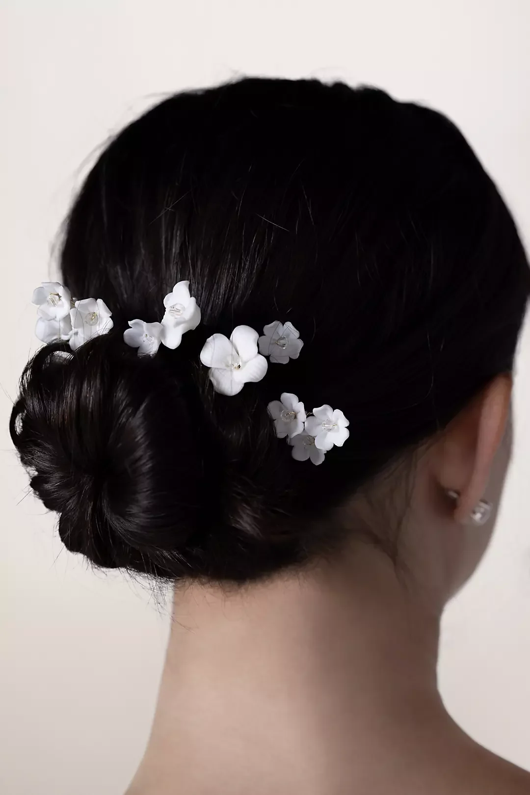 Back view of a woman with dark hair styled in a bun and decorated with small white flowers.