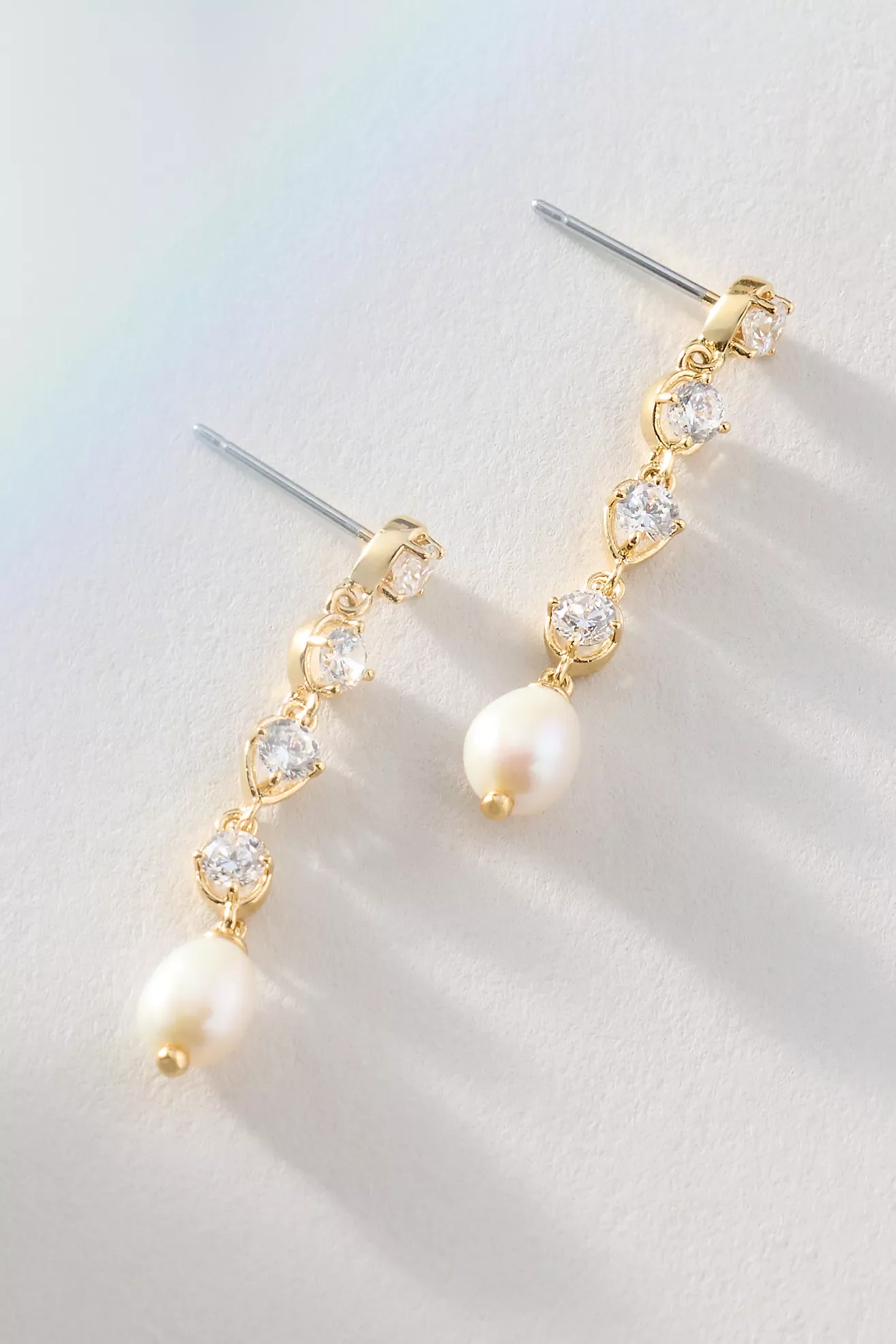 Gold and silver earrings with diamond-like stones and pearl drops placed on a white surface.