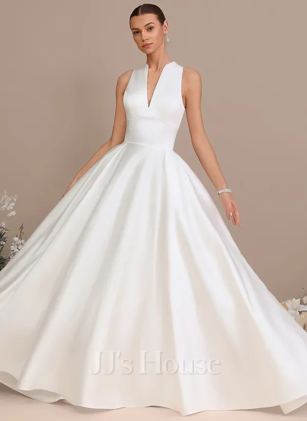 Model wearing a white sleeveless wedding dress with a deep V neckline and a full skirt, standing against a neutral background.