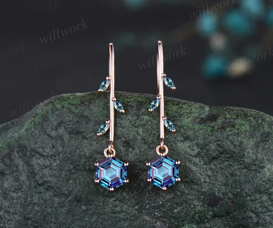 Pair of dangling earrings with blue gemstone accents, hanging over a dark textured rock.