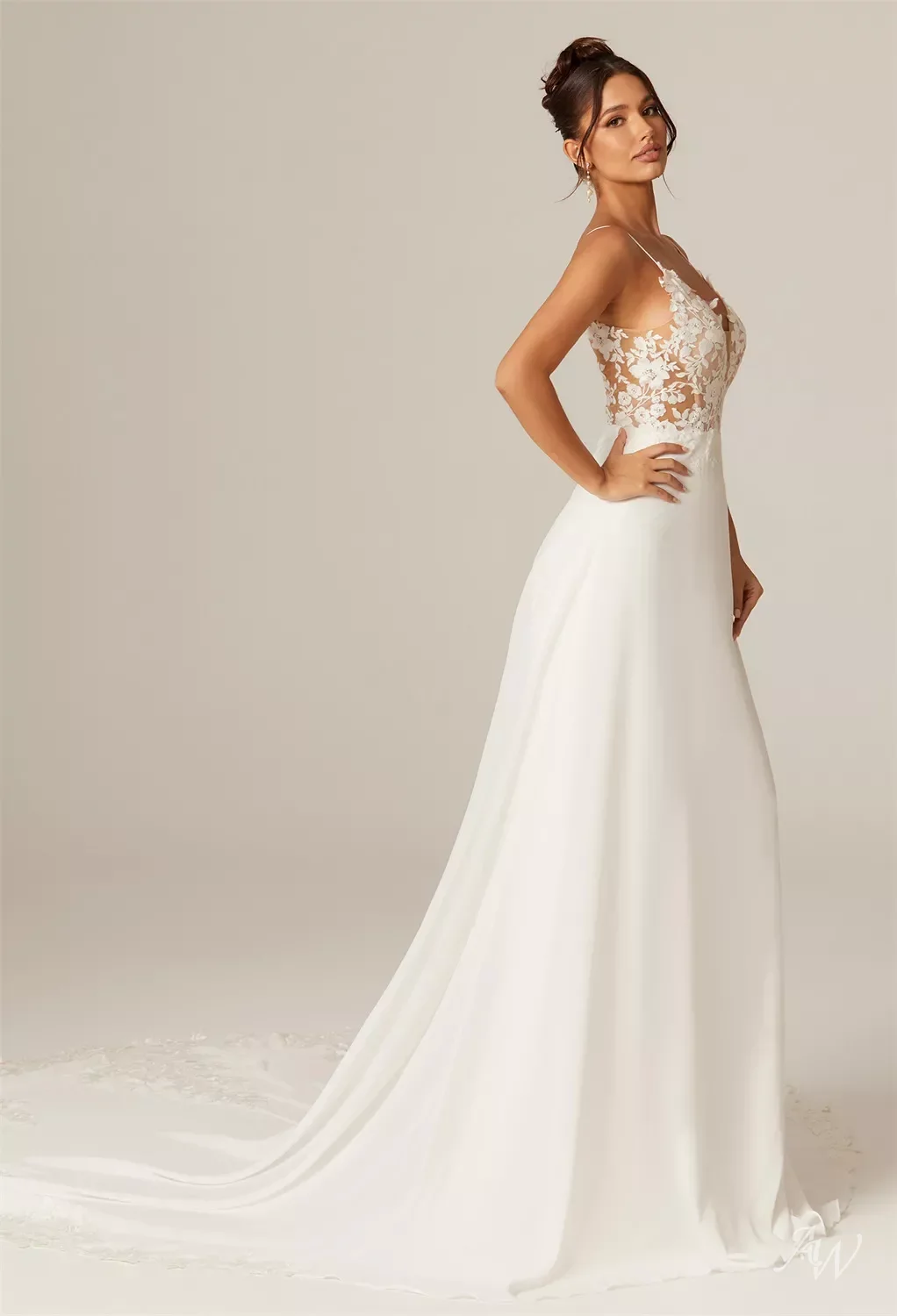 Brunette woman in a wedding dress with a lace floral bodice and a long satin skirt, standing in profile against a neutral background.