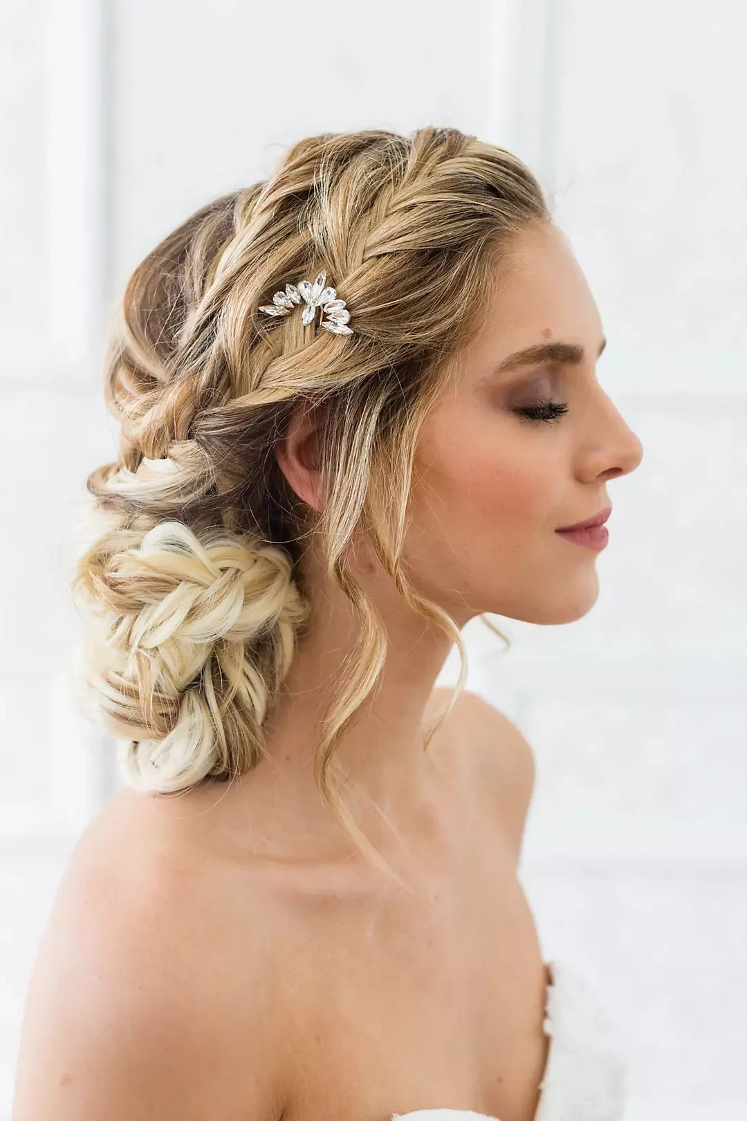Brunette woman with styled hair, adorned with a decorative hairpiece, has her eyes closed and a slight smile, in profile.