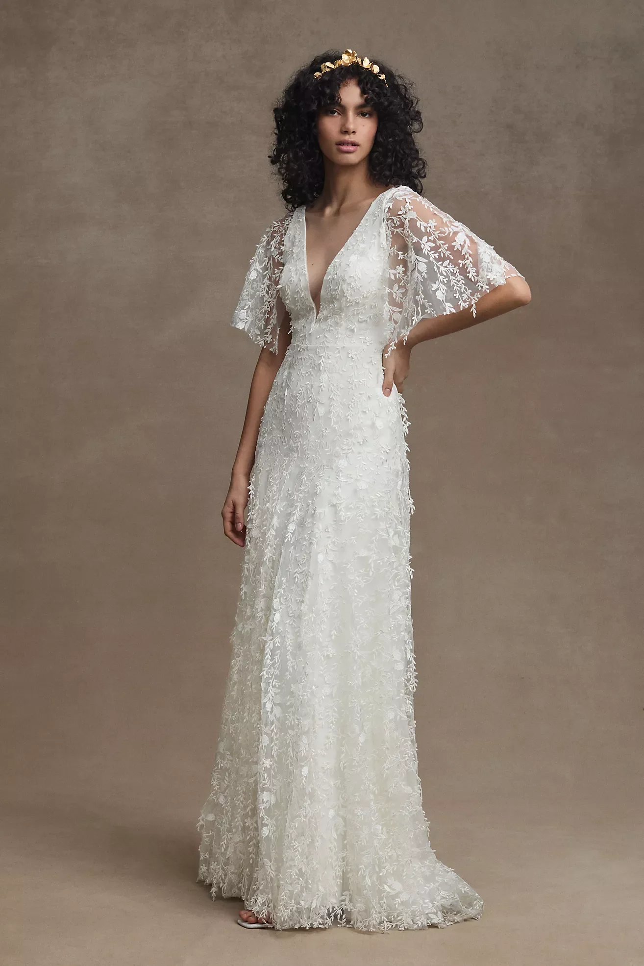 Woman modeling a white lace wedding dress with floral embroidery and sheer lace sleeves with floral details.