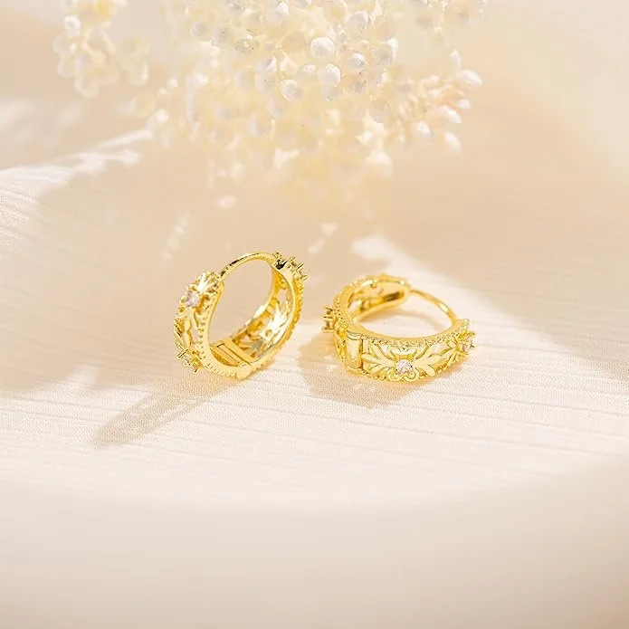 Two gold wedding bands with intricate floral designs and small gemstones, resting on a light-colored surface, with soft lighting and a blurred floral background.