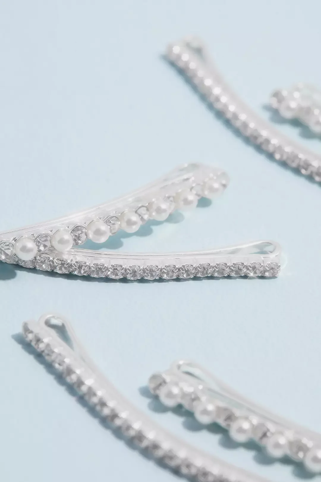Close-up of decorative hair accessories with pearls and rhinestones on a light blue background.