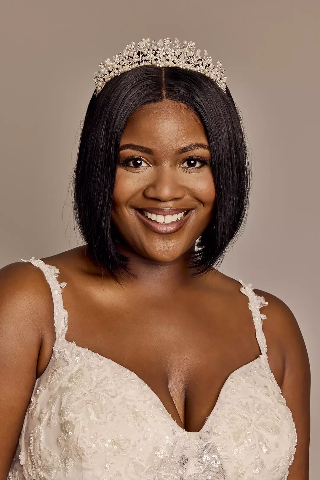 A woman smiling, wearing a wedding dress and a tiara, with shoulder-length black hair.