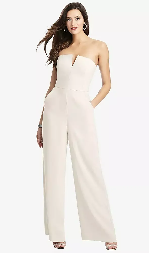 A woman wearing a strapless white jumpsuit with wide-leg pants and a front slit, accessorized with hoop earrings and a bracelet.
